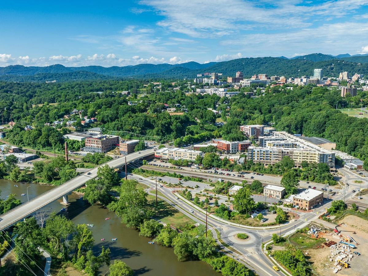 Aerial view of a city surrounded by lush green hills and mountains, with a river, bridges, and clusters of buildings scattered through the landscape.