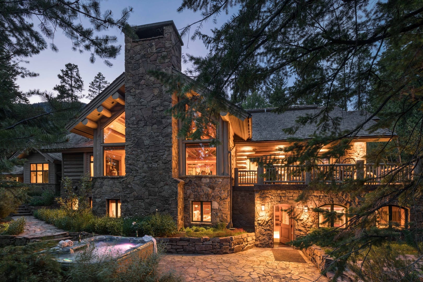 Exterior of stone vacation rental with dim warm lights on inside and trees surrounding area