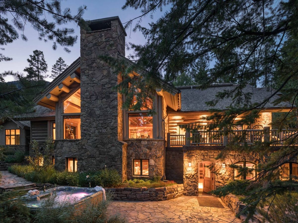 Exterior of stone vacation rental with dim warm lights on inside and trees surrounding area