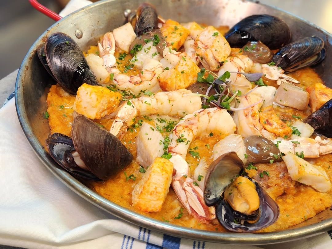 A skillet of seafood paella packed with shrimp, mussels, scallops, and fish topped with fresh herbs. Hook & Barrel serves this flavorful dish with a modern coastal twist in Myrtle Beach.