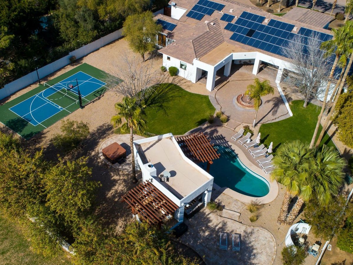 Aerial view of a solar-powered desert estate with a basketball court, resort-style pool, and lush landscaping.