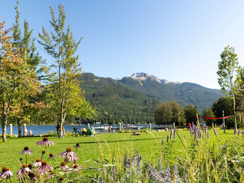 Wildflowers bloom along the grassy shore of Lost Lake with mountain views in the distance. Families relax, bike, and enjoy the peaceful park just minutes from Whistler Village. Lost Lake is a favorite spot for swimming, picnics, and easy nature walks.