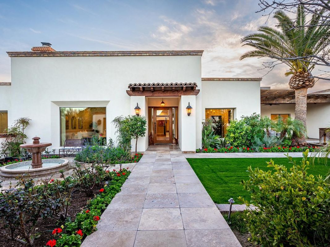 Elegant Mediterranean-style home with lush landscaping, a charming fountain, and warm architectural details.