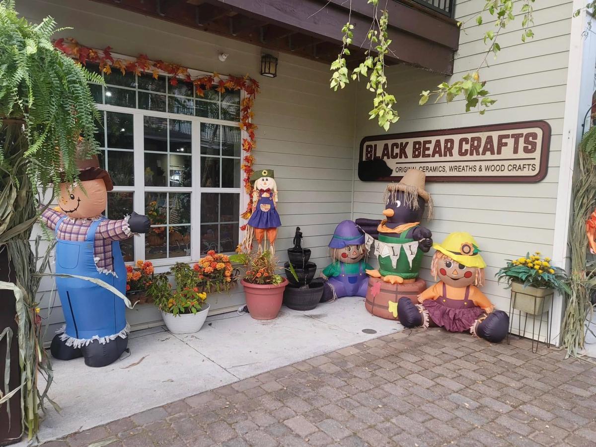 A charming craft shop decorated with fall leaves and cute scarecrow inflatables welcomes visitors with a warm, homey vibe. Bright flowers and outdoor décor add pops of color around the entrance of Black Bear Crafts. It feels like a friendly spot to browse handmade goods in the Smokies.
