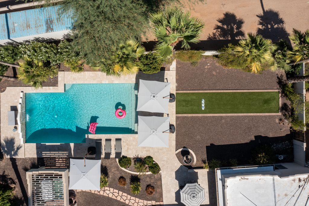 An aerial view of a private backyard oasis showcasing a sleek pool with sun loungers, shaded seating, and a putting green set within thoughtfully landscaped desert surroundings.