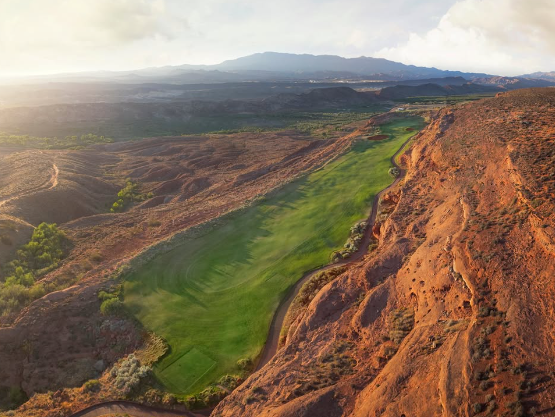A stunning aerial view of a golf course nestled between red rock cliffs and desert terrain, with lush green fairways contrasting the rugged landscape