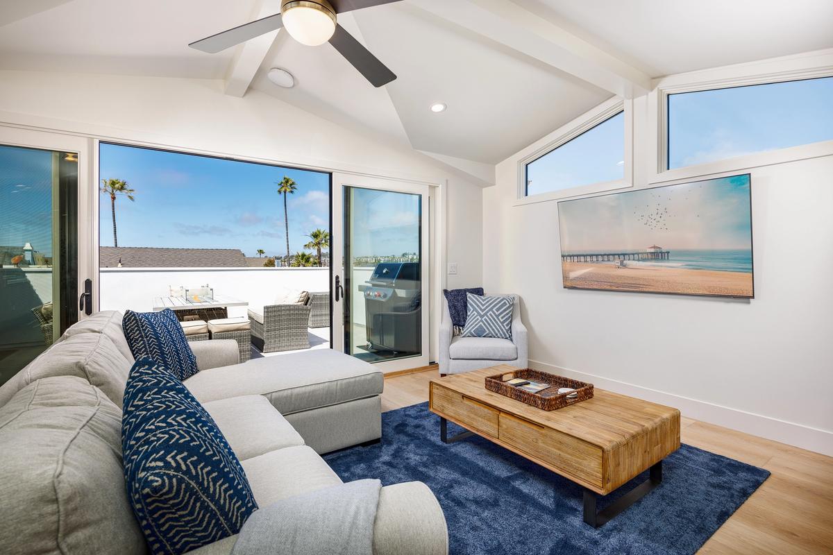 A bright coastal living room opens to a sunlit balcony with ocean views and palm trees. The airy design, modern décor, and outdoor space show what luxury vacation rentals can offer beyond standard Airbnbs.