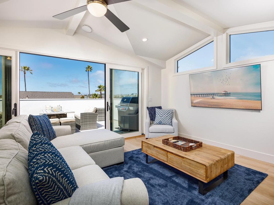 A bright coastal living room opens to a sunlit balcony with ocean views and palm trees. The airy design, modern décor, and outdoor space show what luxury vacation rentals can offer beyond standard Airbnbs.