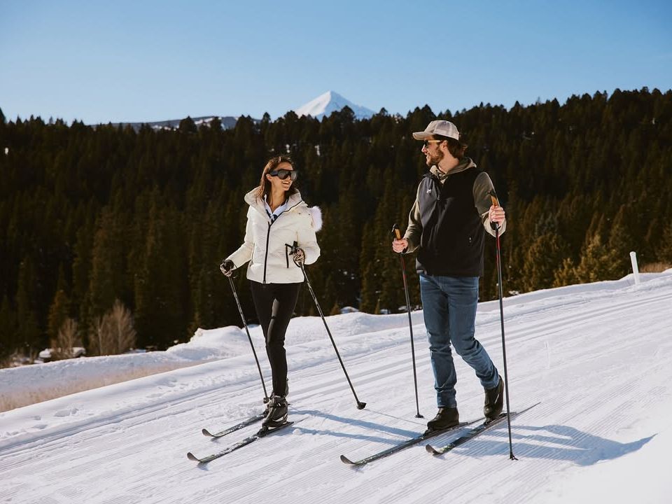 A couple cross-country skiing together in Big Sky with Lone Peak rising in the background. Winter trails here combine exercise, fresh air, and stunning scenery.