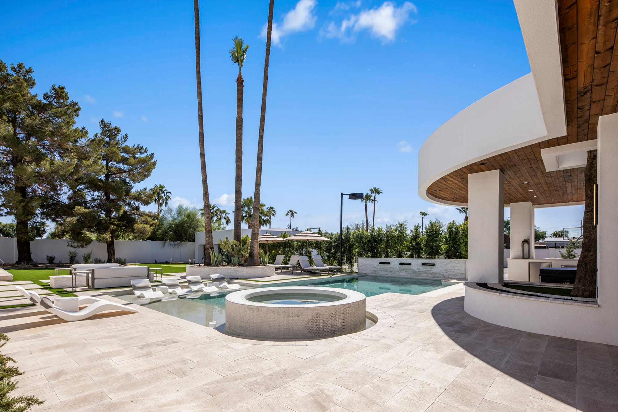 Sleek backyard pool and spa area at a modern vacation rental with curved architecture, palm trees, and in-water lounge chairs. The clean design and open patio make this outdoor space feel bright, stylish, and made for relaxing in the sun.