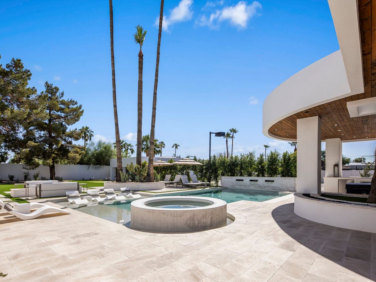 Sleek backyard pool and spa area at a modern vacation rental with curved architecture, palm trees, and in-water lounge chairs. The clean design and open patio make this outdoor space feel bright, stylish, and made for relaxing in the sun.