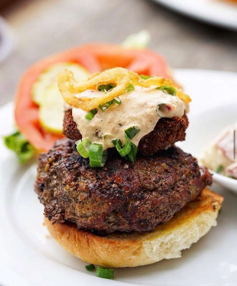 A juicy gourmet burger topped with crispy onions and creamy sauce from Poe’s Tavern. This classic beachside spot is known for its creative burgers, craft beer, and laid-back coastal charm.