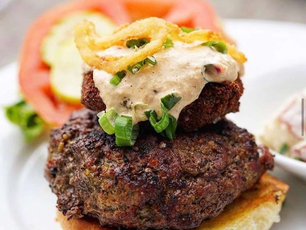 A juicy gourmet burger topped with crispy onions and creamy sauce from Poe’s Tavern. This classic beachside spot is known for its creative burgers, craft beer, and laid-back coastal charm.