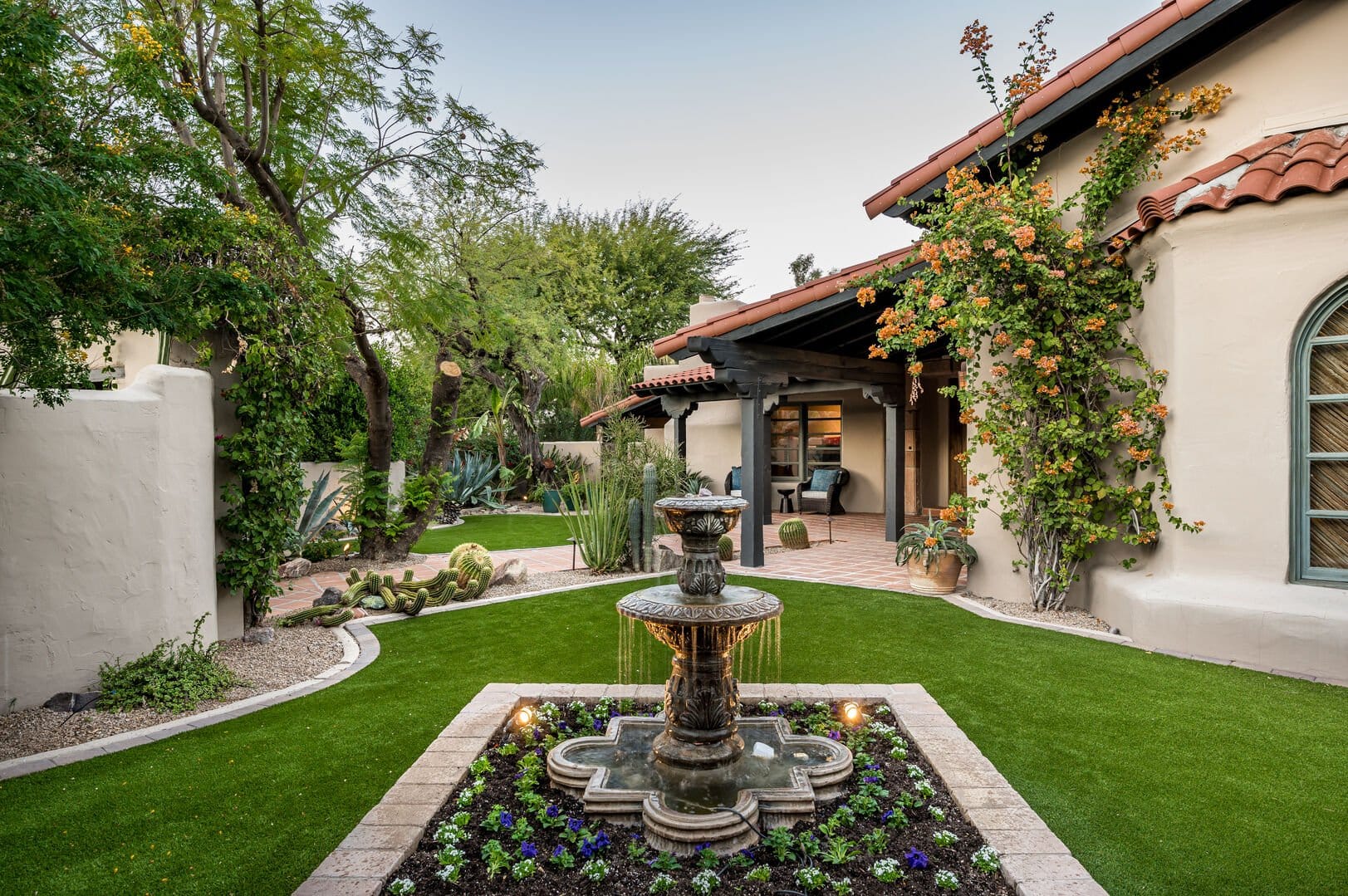 Charming Spanish-style courtyard with lush greenery, a flowing tiered fountain, and rustic architectural details.