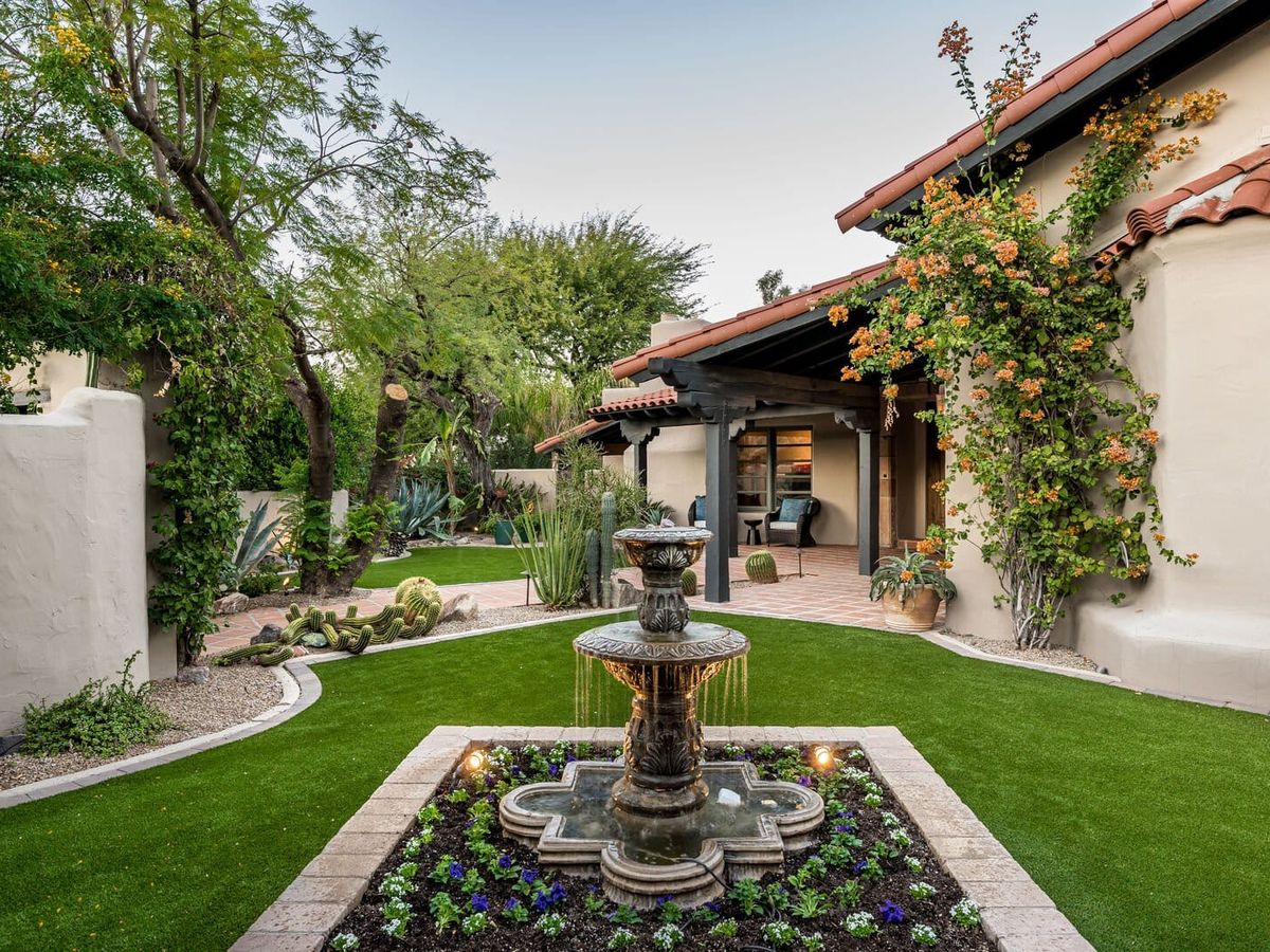 Charming Spanish-style courtyard with lush greenery, a flowing tiered fountain, and rustic architectural details.
