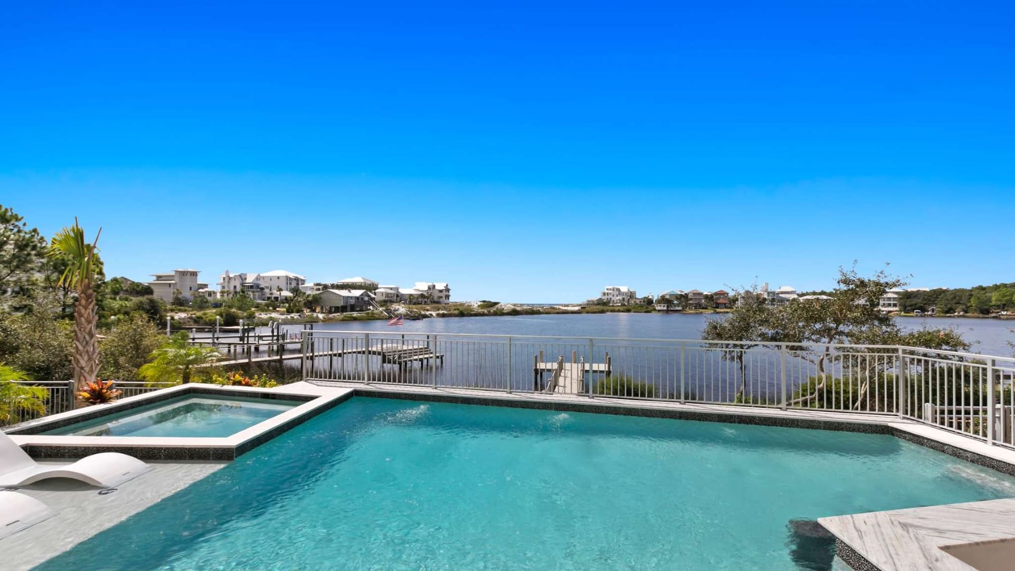 A private waterfront pool overlooks a peaceful coastal lagoon surrounded by upscale beach homes. Clear blue water and sunny skies make this outdoor space perfect for a relaxing vacation day.