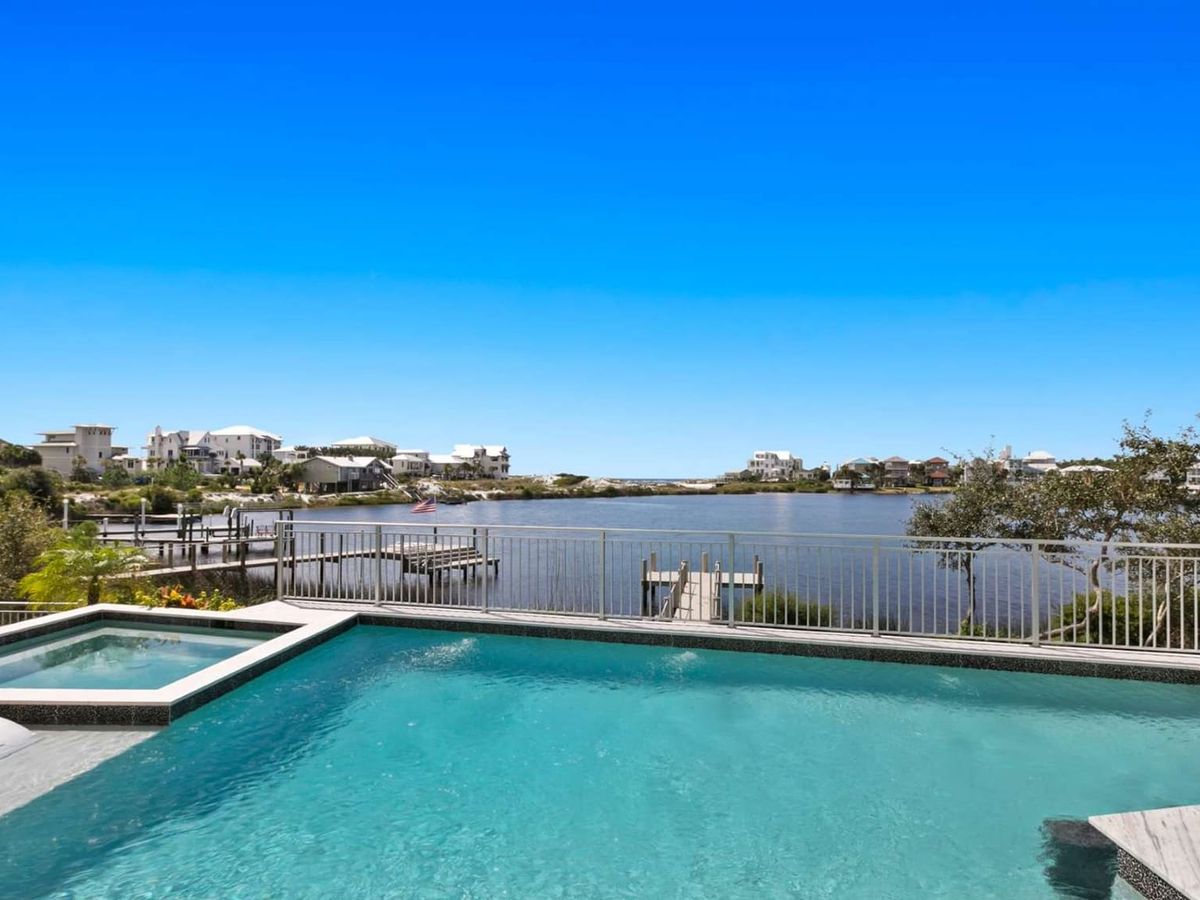 A private waterfront pool overlooks a peaceful coastal lagoon surrounded by upscale beach homes. Clear blue water and sunny skies make this outdoor space perfect for a relaxing vacation day.