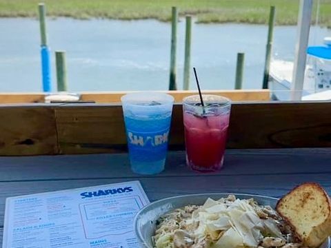 A plate of pasta and colorful drinks sit by the window at Sharky’s Waterfront Bar and Grill with marsh views outside. This relaxed setting is perfect for casual waterfront dining.