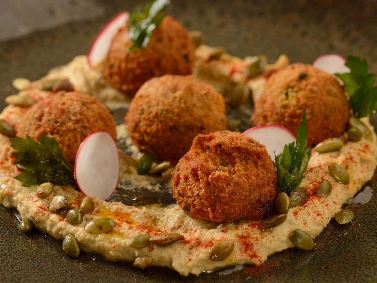 Crispy falafel balls served on creamy hummus with radish slices and pumpkin seeds at Jungle Navigation Co. LTD Skipper Canteen. A flavorful plant-based appetizer