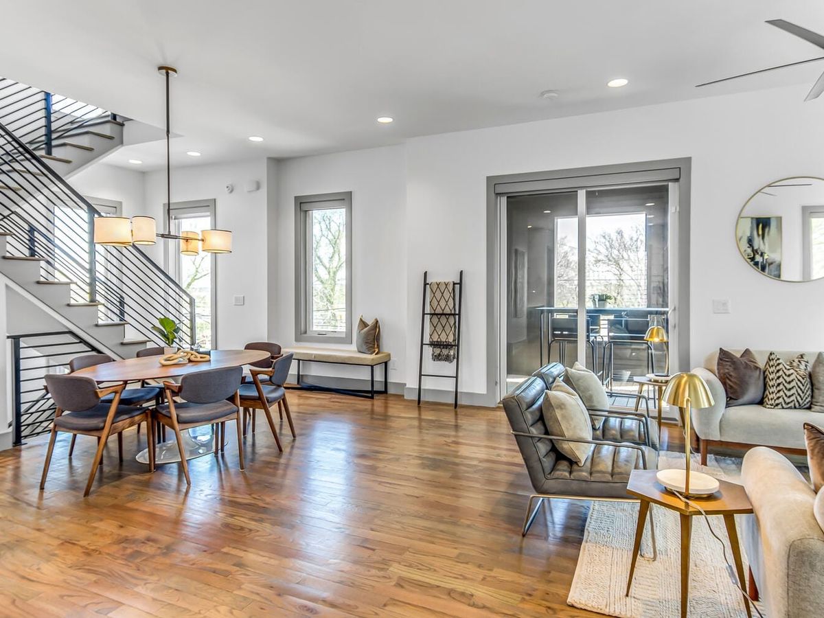 A modern living room in downtown Nashville with floor-to-ceiling windows, sleek furniture, and an open balcony. Pops of art and city views bring a mix of urban energy and cozy comfort.
