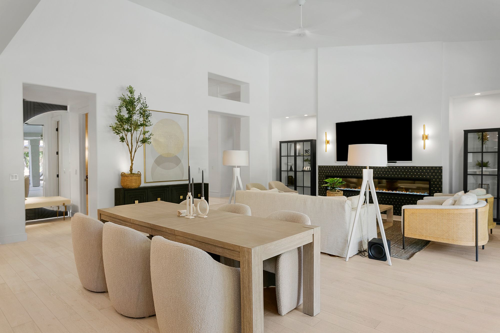 An elegant open-concept living and dining space with soaring ceilings, soft neutral finishes, a modern fireplace, and curated furnishings that create a warm, sophisticated atmosphere.