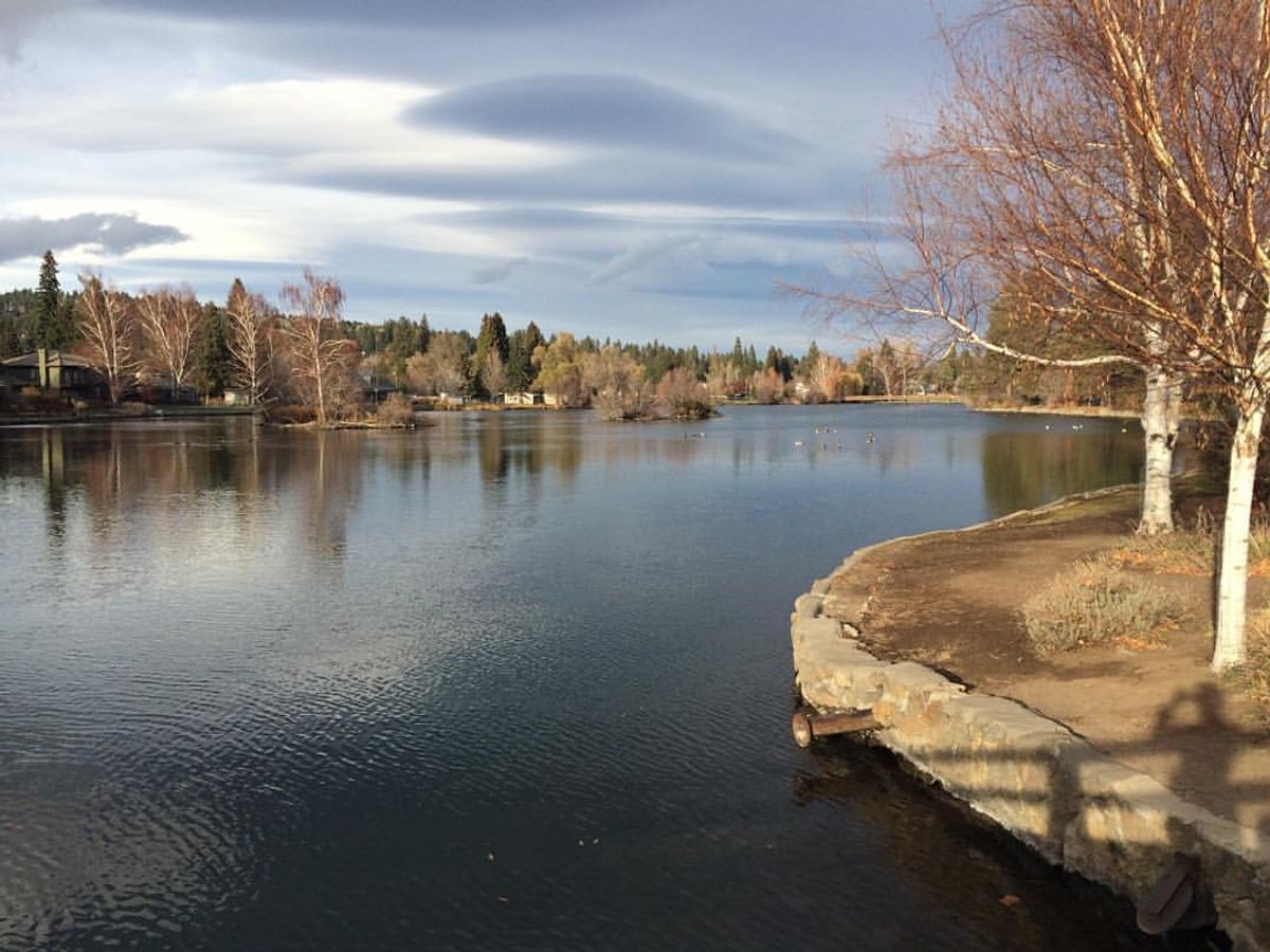Peaceful view of Drake Park’s Mirror Pond, with calm waters framed by bare trees and soft cloud cover.