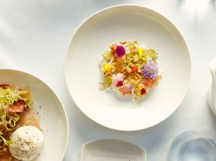 A beautifully plated garden salad topped with edible flowers and a gourmet cheese dish beside it. Ideal for a fresh, light lunch at an elegant spot.