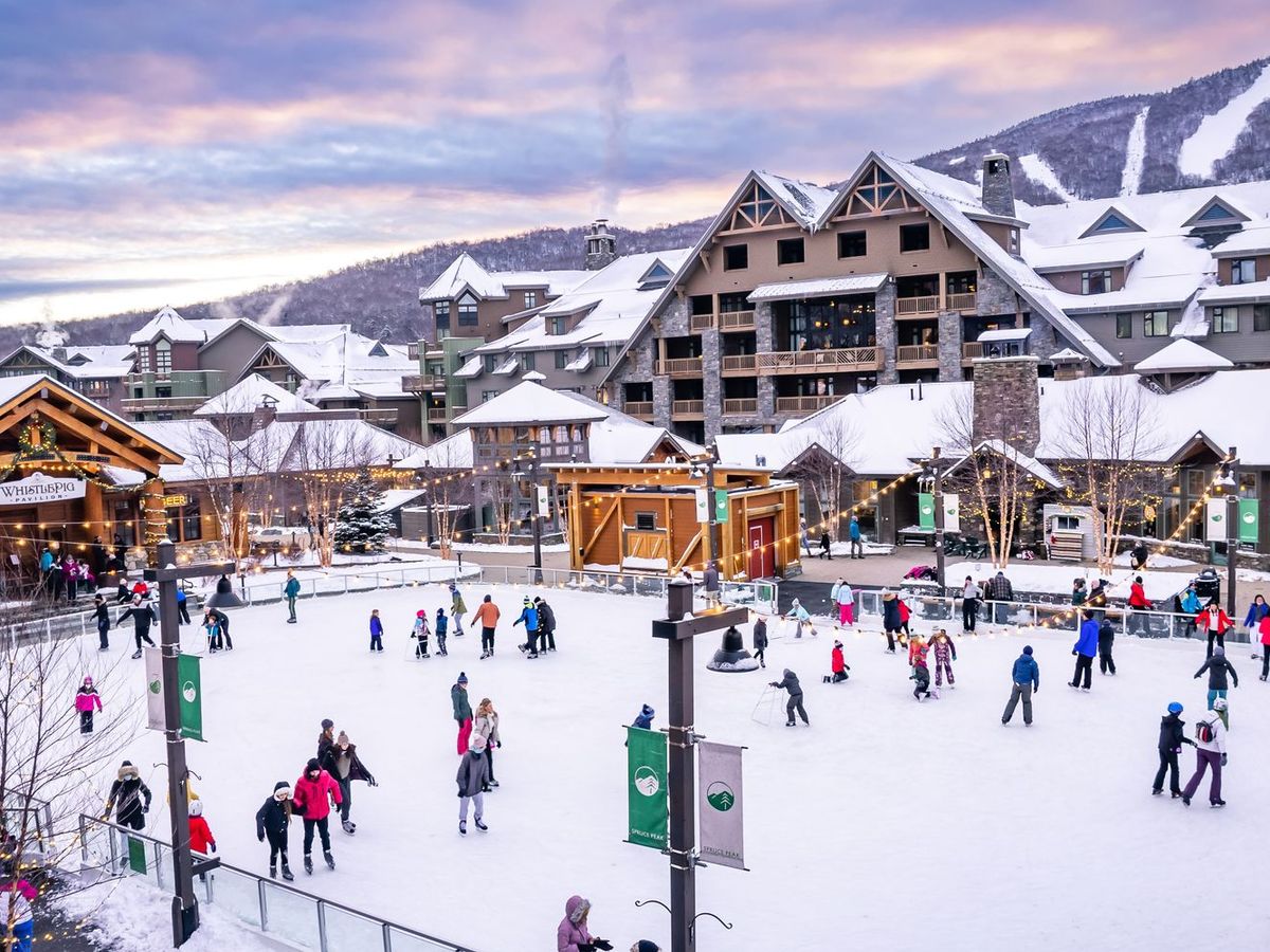 Families skate across an outdoor ice rink in Stowe, Vermont, surrounded by alpine lodges twinkling with winter lights. Snowy slopes rise in the background, creating a festive mountain-town atmosphere. File Name: Stowe | Vacation Rentals
