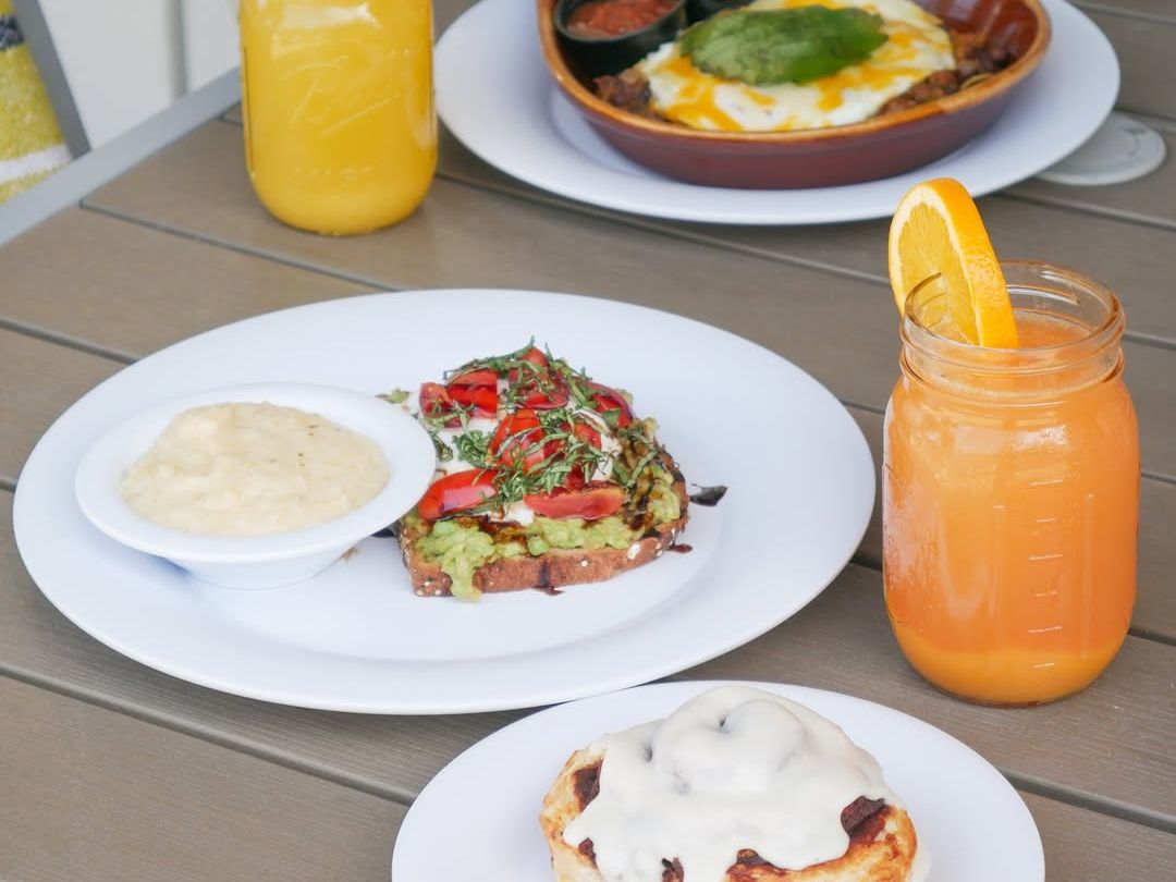 A colorful brunch spread at Crackings with avocado toast, grits, cinnamon roll, and mimosas. A fresh and flavorful way to start your day in Destin.