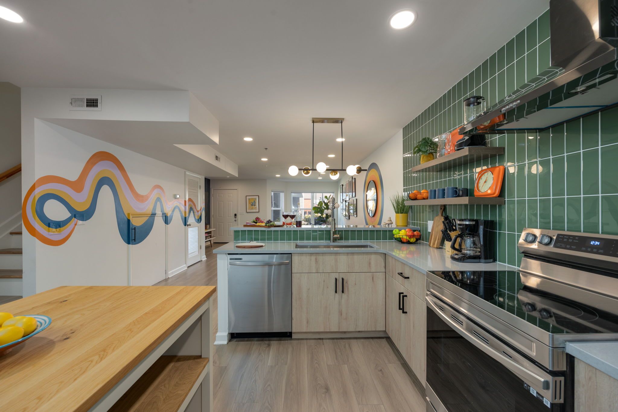 A vibrant, retro-inspired kitchen with green tile backsplash, open shelving, stainless steel appliances, and a colorful wave mural flowing through the space, creating a playful yet polished Nashville retreat.