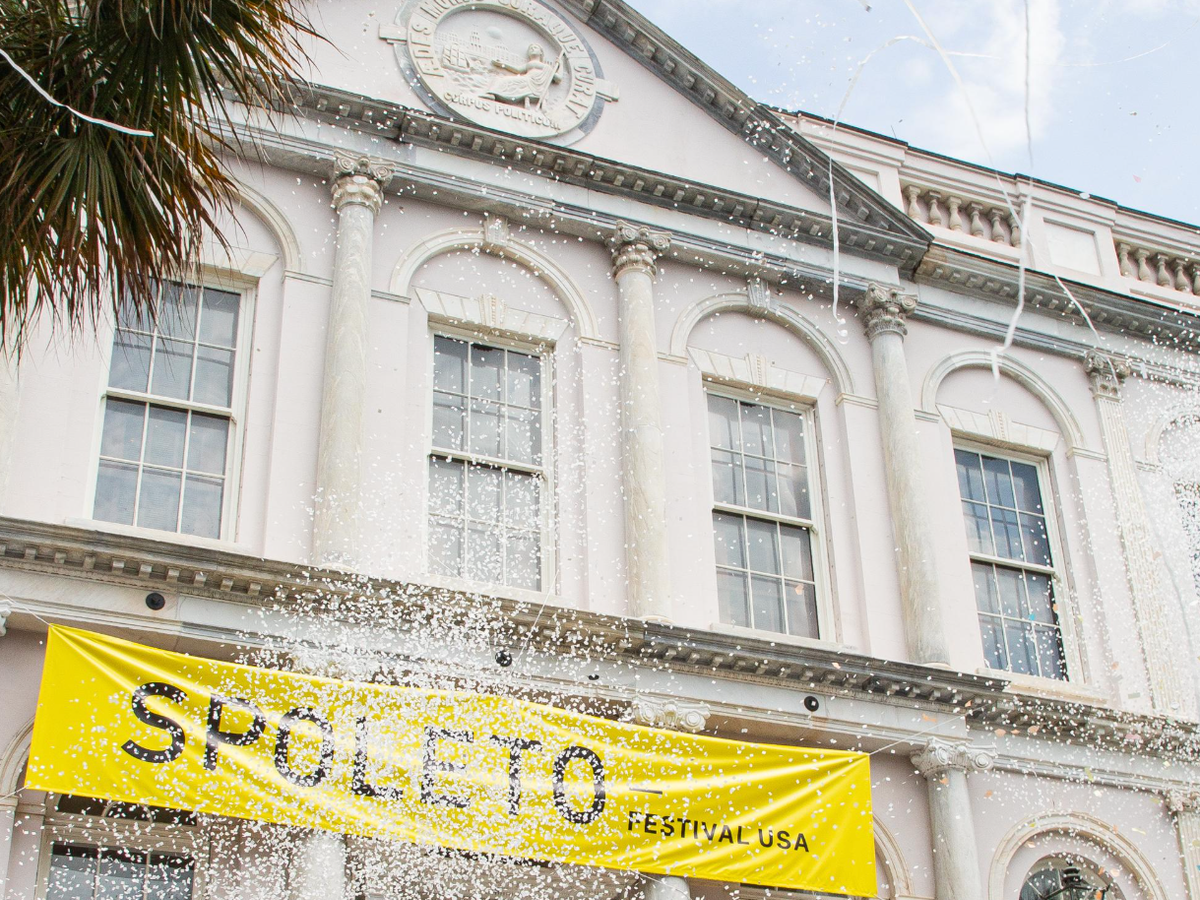 Yellow banner on building that spells Spoleto with white confetti falling in front of it