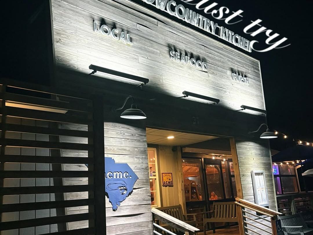 The cozy front entrance of Acme Lowcountry Kitchen at night, with rustic wood siding and soft lighting that draws you in. A local seafood spot that’s as warm and welcoming as the food is fresh.