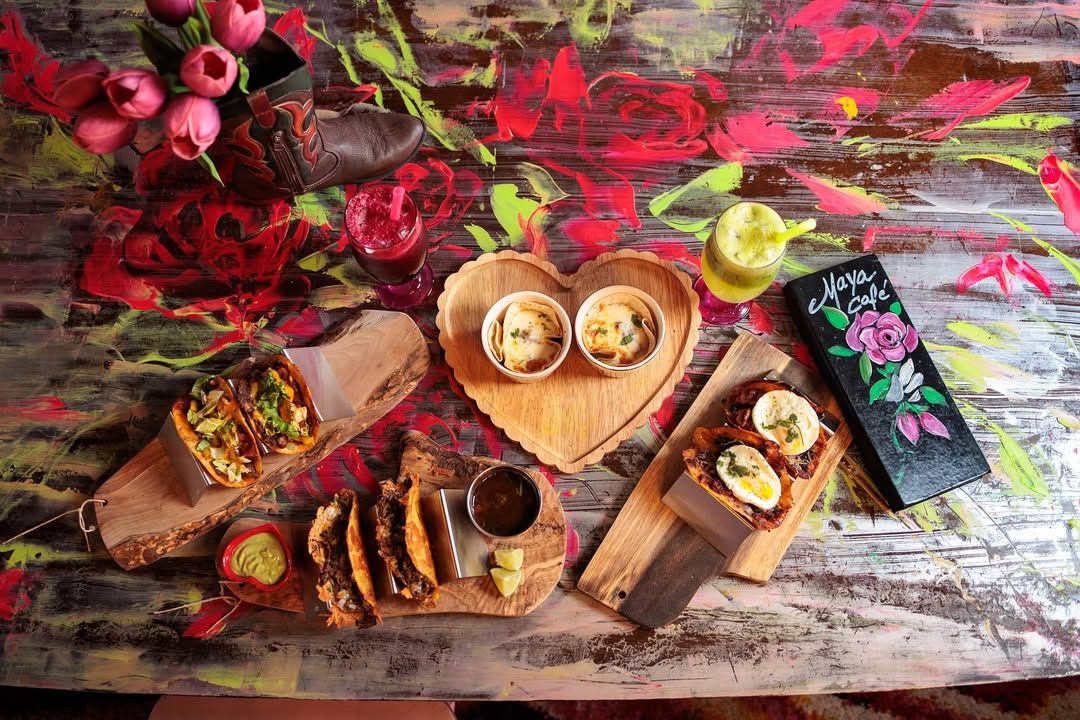 Bright tacos, dips, and fresh juices sit on an artsy floral table covered in bold colors and textures. The food feels fun, creative, and full of personality, matching the playful vibe of the café. It’s the kind of spot that makes every meal feel like a little celebration.