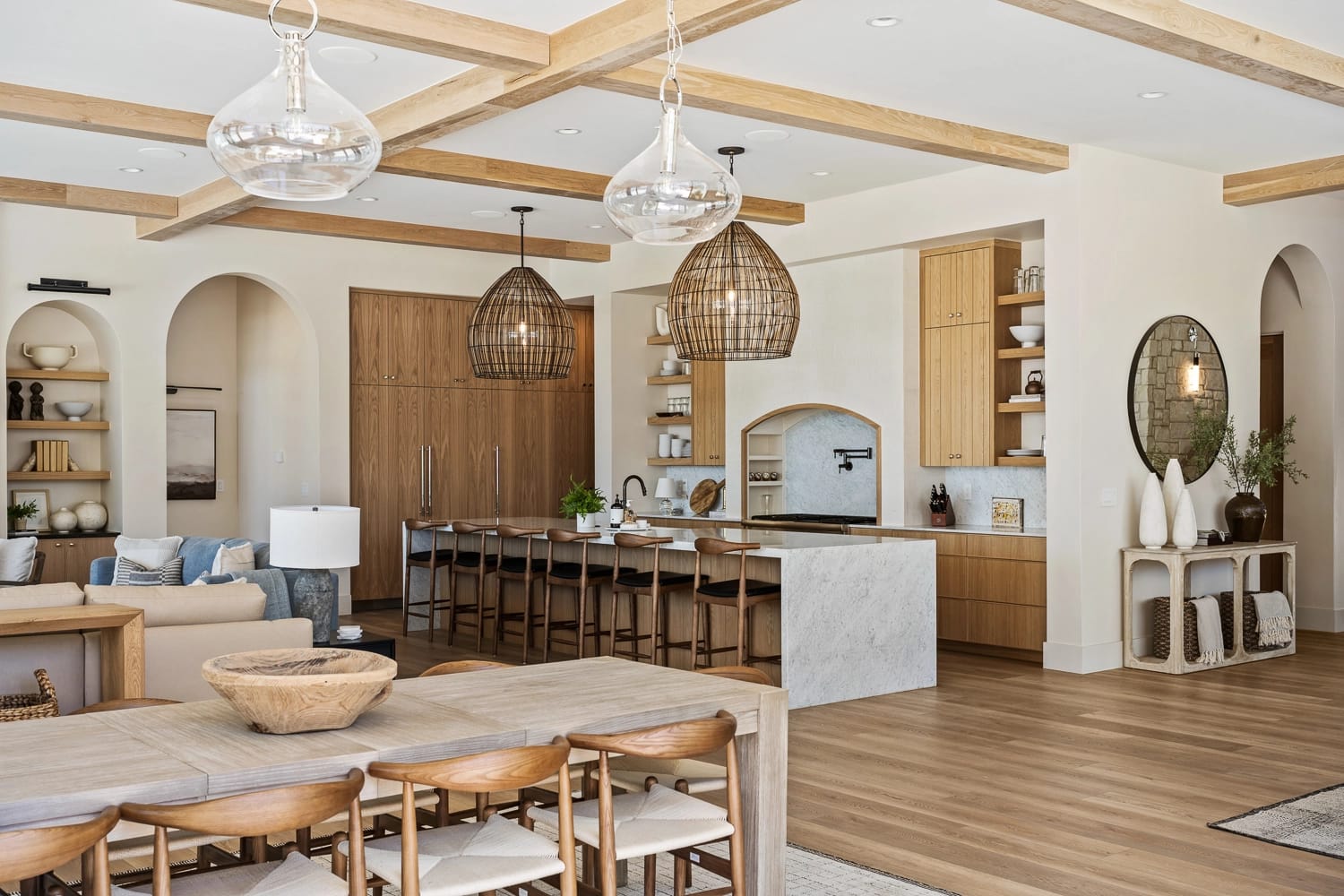 Open-concept living space featuring a modern kitchen with wood cabinetry, a large island with bar seating, and stylish woven pendant lights.