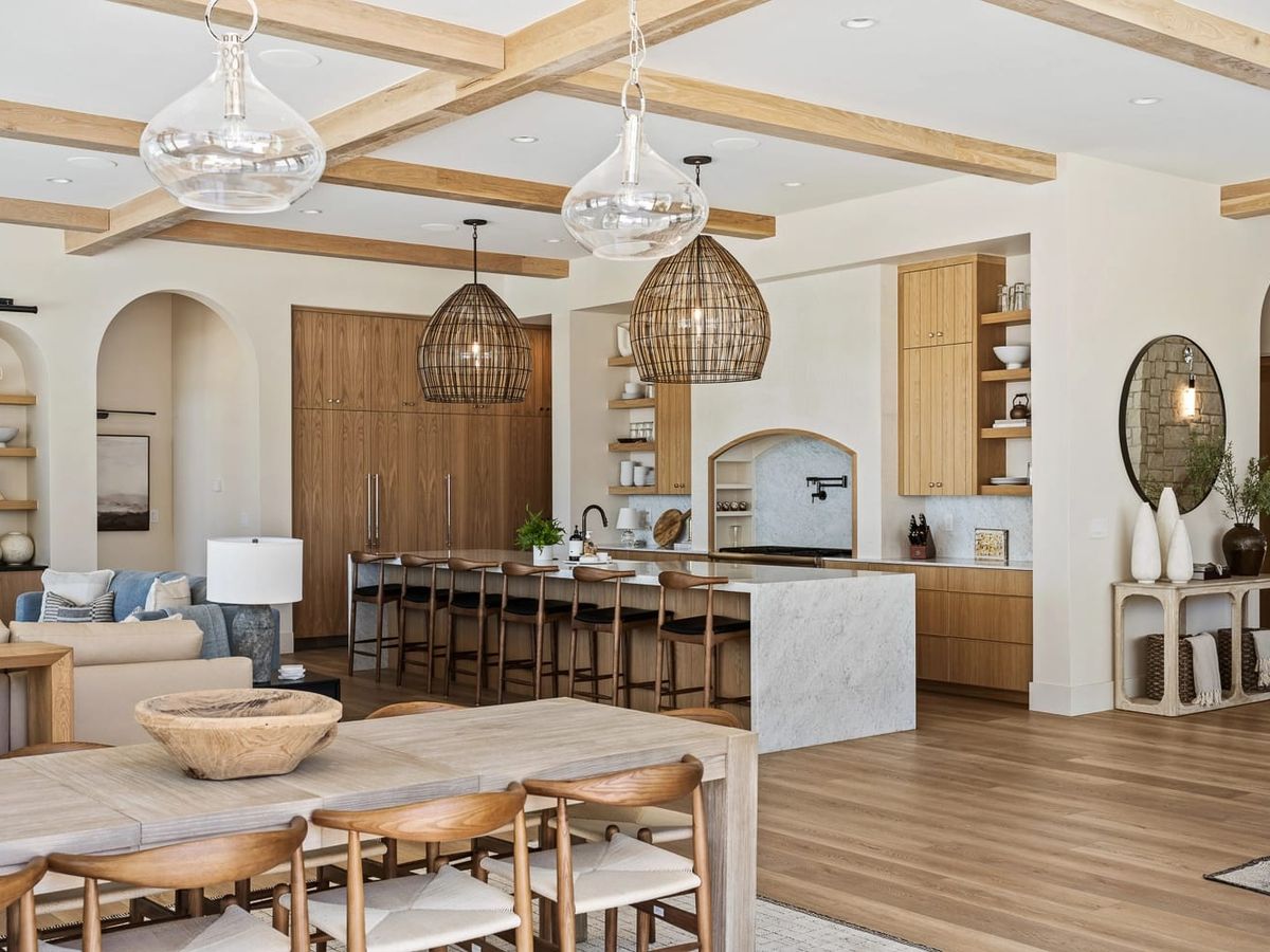 Open-concept living space featuring a modern kitchen with wood cabinetry, a large island with bar seating, and stylish woven pendant lights.