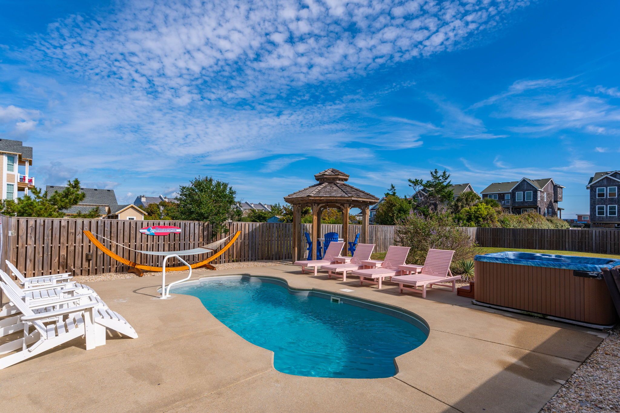 Private pool next to pink chairs and hot tub with hammock and white chairs