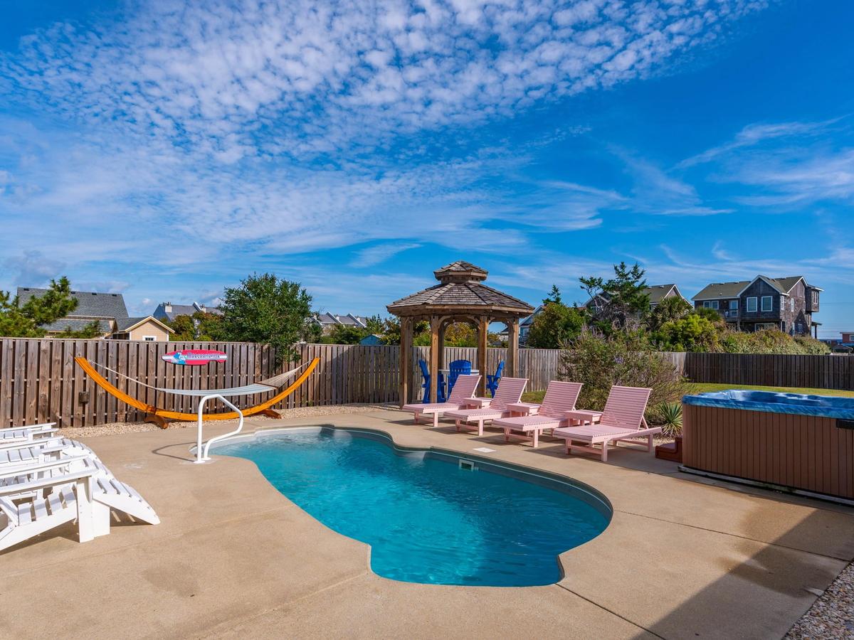 Private pool next to pink chairs and hot tub with hammock and white chairs