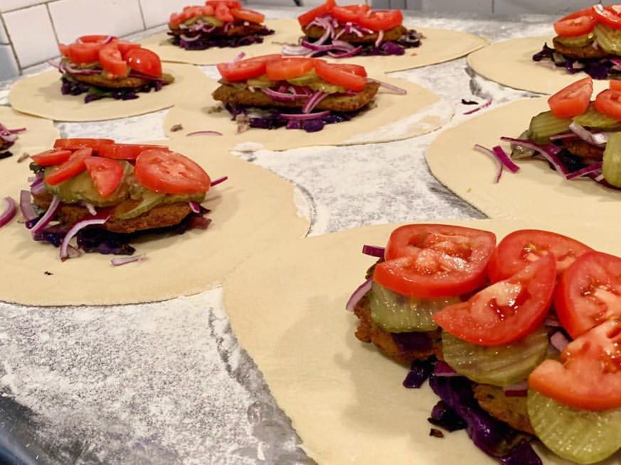 Freshly made Cornish pasties filled with pickles, tomatoes, onions, and seasoned meat, laid out on a floured prep table. The hearty, hand-held pies highlight the restaurant’s specialty comfort food.