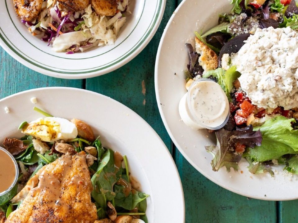 Fresh and colorful plates from Gnat’s Landing show off grilled chicken, blackened shrimp, and house-made chicken salad over leafy greens. A casual, flavorful bite with island charm.