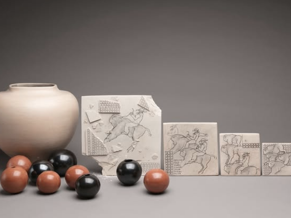 A collection of handcrafted ceramic tiles featuring etched illustrations of riders on animals is displayed alongside a smooth beige vase and glossy spherical beads in black and terracotta colors.