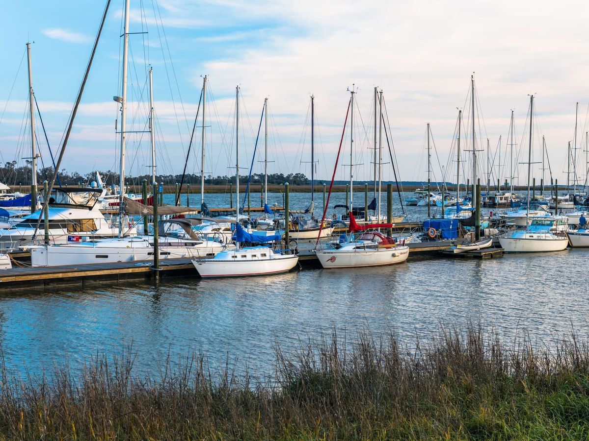A marina filled with sailboats sits along the calm waterfront of St. Simons Island, Georgia. Tall masts reflect on the water while marsh grass lines the shoreline. St. Simons Island offers relaxed coastal living and scenic harbor views.