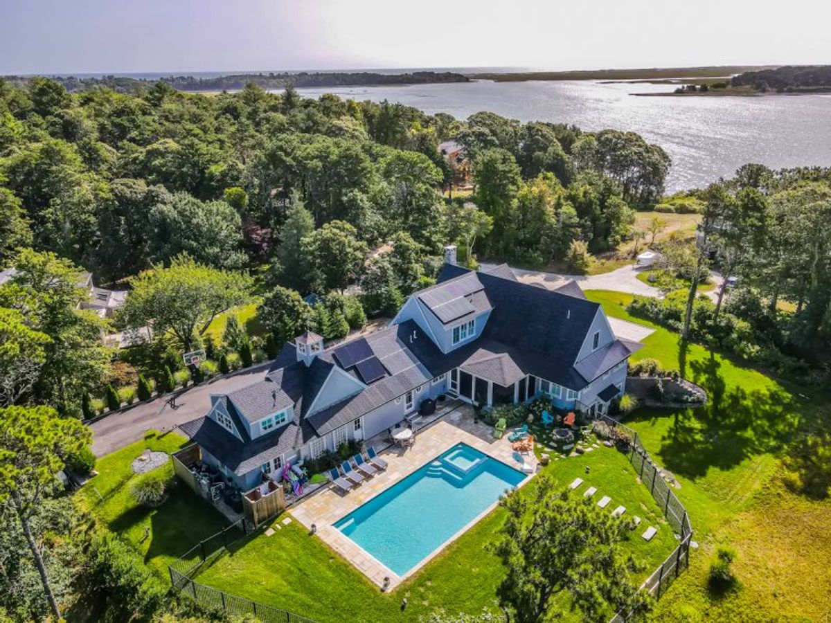 Aerial view of a spacious coastal estate surrounded by lush greenery, featuring a private backyard pool, expansive lawn, and scenic waterfront vistas stretching beyond the property.