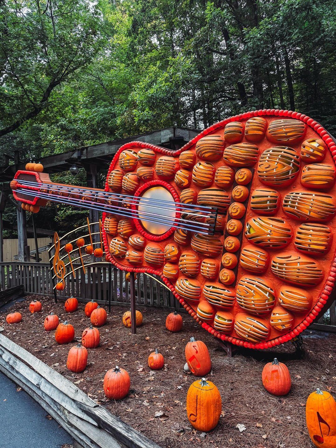 A giant guitar made of orange pumpkins stands at Dollywood surrounded by smaller pumpkins and trees. The festive fall display celebrates the park’s love for music and autumn fun.