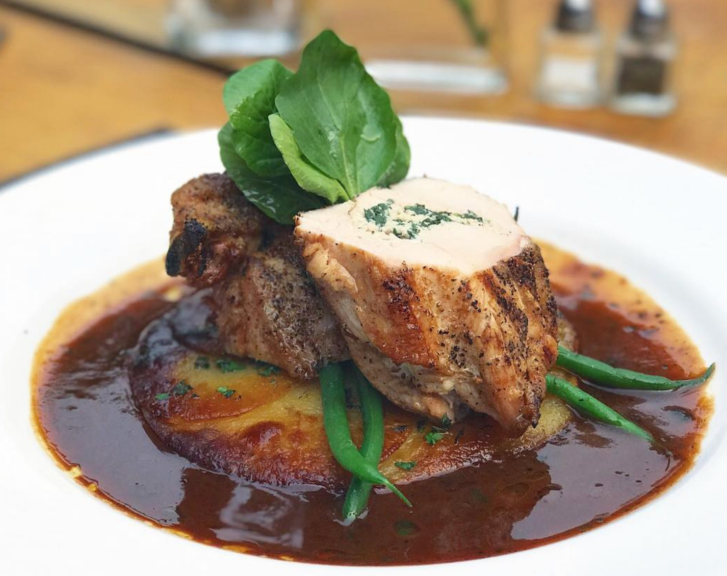 Plated seared chicken breast topped with herb butter, served over a crisp potato cake with green beans and finished in a rich brown sauce.