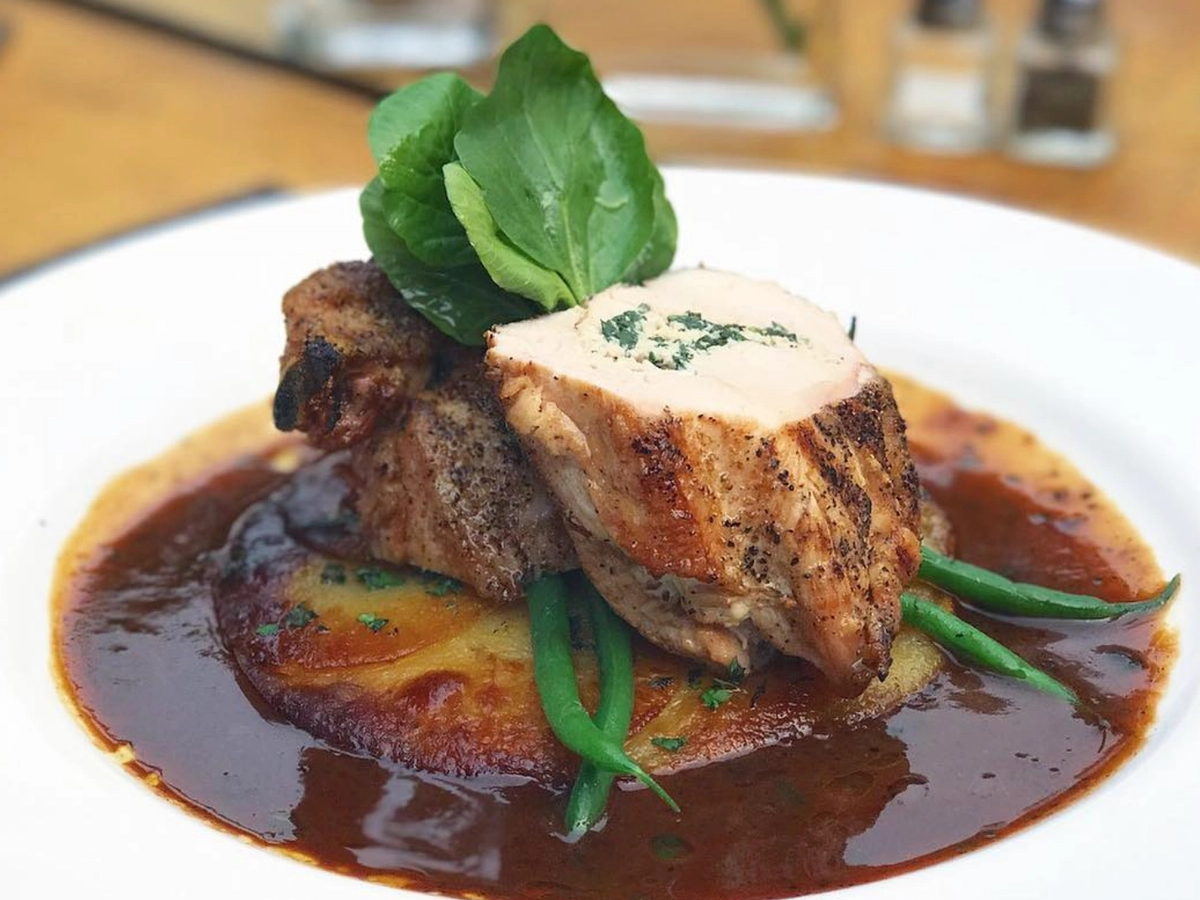 Plated seared chicken breast topped with herb butter, served over a crisp potato cake with green beans and finished in a rich brown sauce.