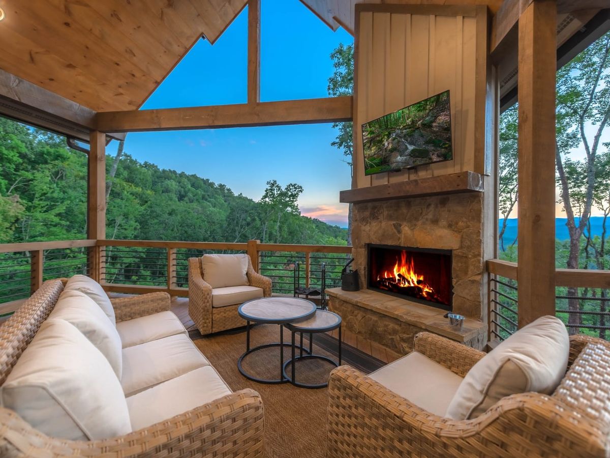 Cozy outdoor living space with plush wicker seating, a stone fireplace, and a sunset view over the mountains. Perfect spot for late-night talks and morning coffee with nature all around.