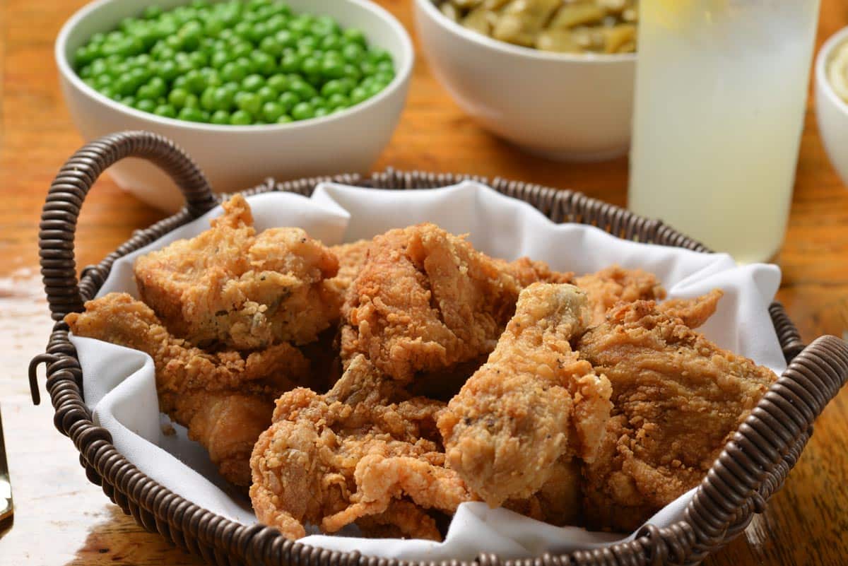 A basket of golden, crispy fried chicken served family-style with sides of peas and green beans. The classic Southern comfort food setting invites guests to share hearty meals and warm company.