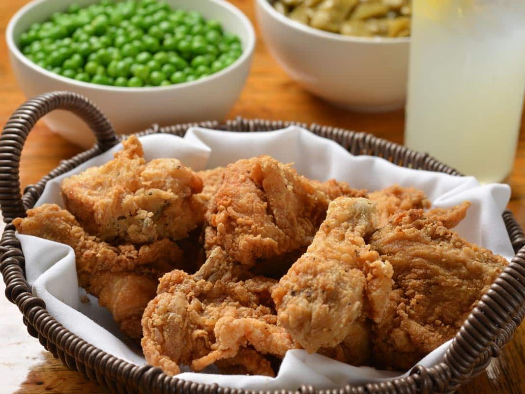 A basket of golden, crispy fried chicken served family-style with sides of peas and green beans. The classic Southern comfort food setting invites guests to share hearty meals and warm company.
