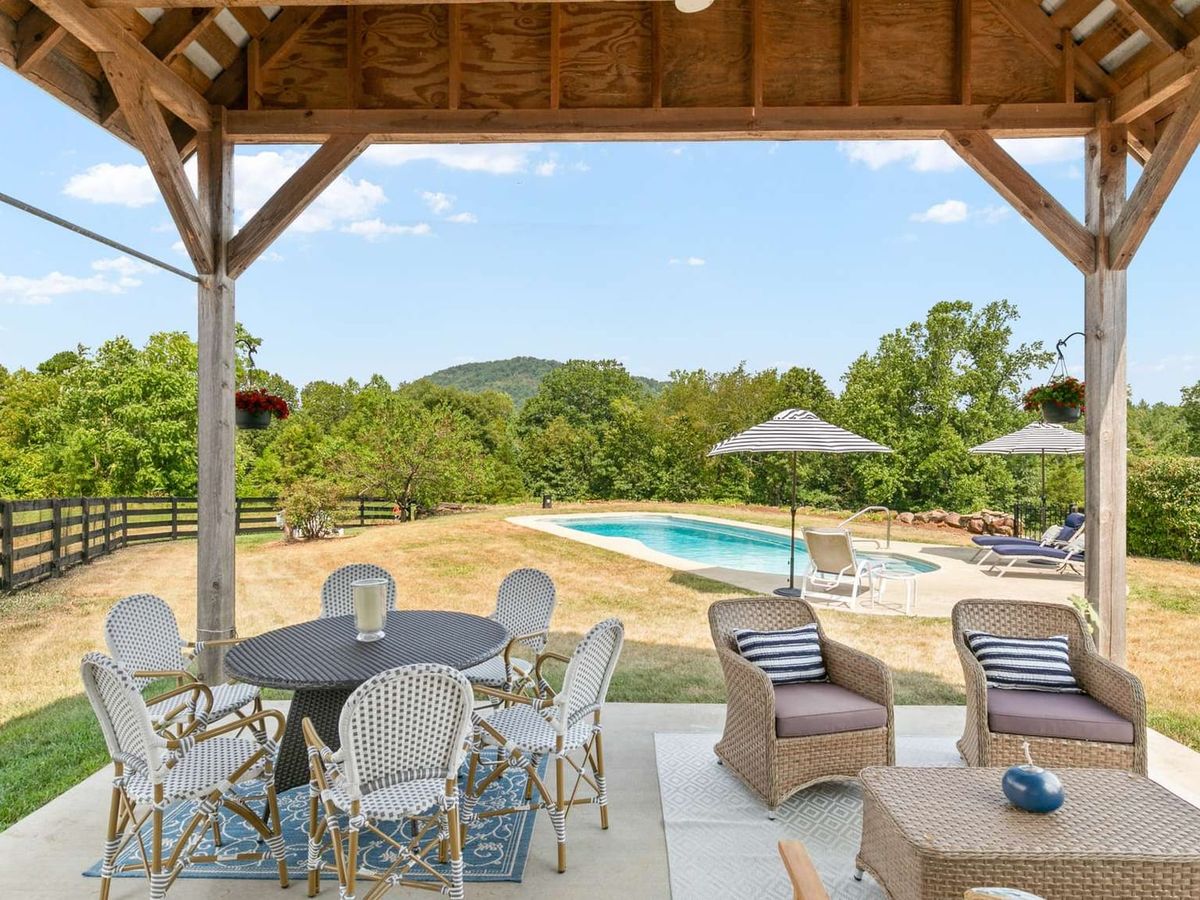 A dark wood farmhouse with green metal roofing sits under a canopy of fall foliage. Barn-style doors and rustic charm make this retreat a warm and inviting place to escape the city.