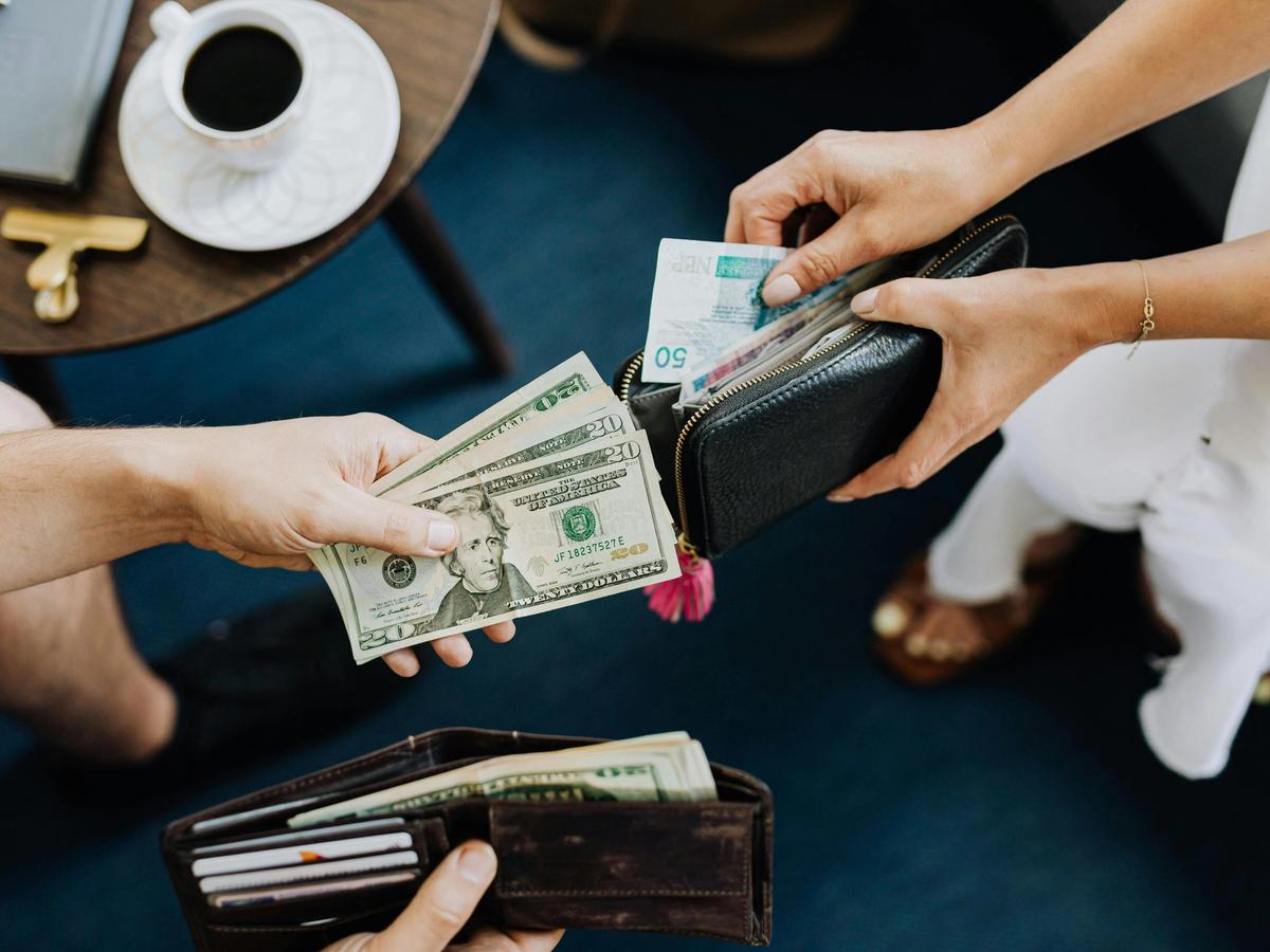 Travelers exchanging U.S. dollars and Mexican pesos, a reminder to prepare local currency when visiting Huatulco. A coffee table and wallets create a casual travel moment.